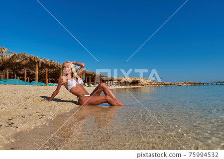 Young fashion woman sitting on the beach shore Young fashion woman sitting on the beach shore 75994532