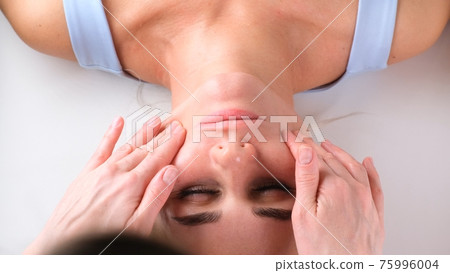 Facial massage beauty treatment. Close up of a young womans face lying on back, getting face lifting 75996004
