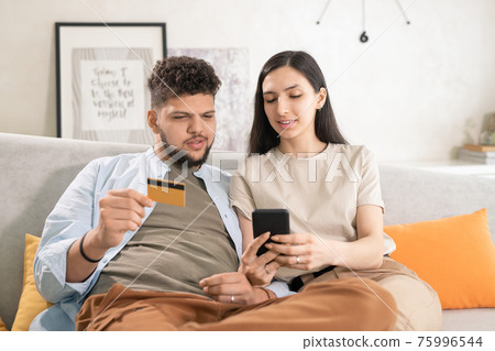 Young brunette woman showing tasty food in smartphone to her husband with credit card Young brunette woman showing tasty food in smartphone to her husband with credit card 75996544