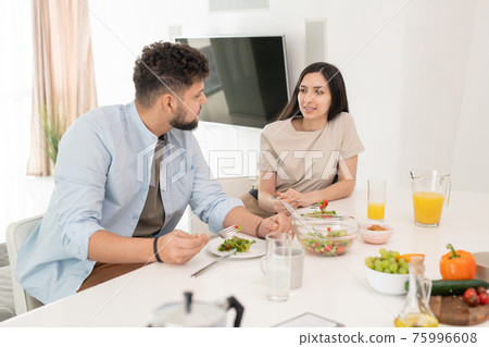 Young brunette woman looking at her husband during conversation by breakfast in the morning Young brunette woman looking at her husband during conversation by breakfast in the morning 75996608