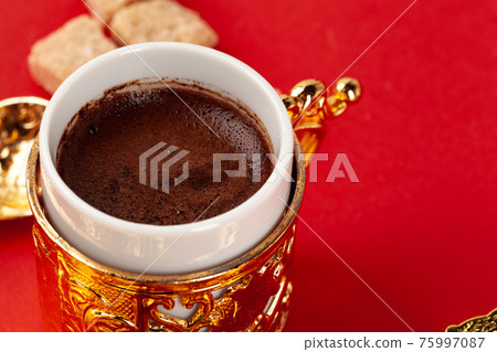 Turkish coffee in a golden oriental cup on red background Turkish coffee in a golden oriental cup on red background 75997087