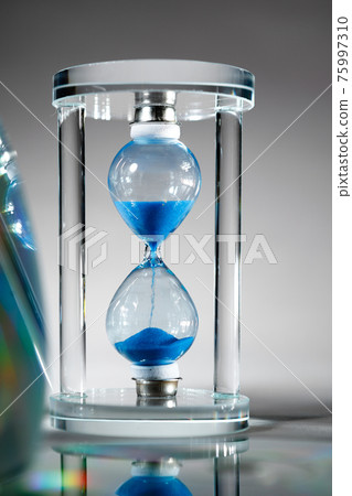Blue hourglass on gray background close up Blue hourglass on gray background close up 75997310