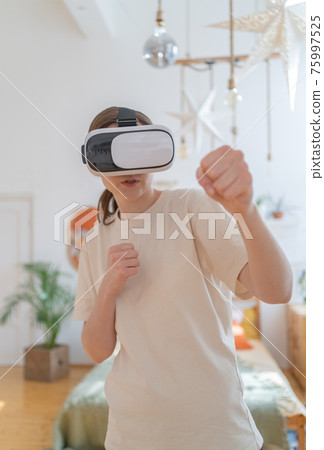 Virtual sports. Fitness at home. Young slender woman trains in virtual reality helmet Virtual sports. Fitness at home. Young slender woman trains in virtual reality helmet 75997525