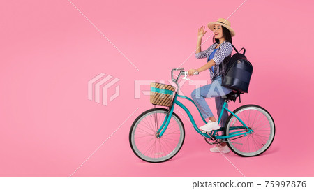 Excited asian woman riding bicycle waving hand 75997876