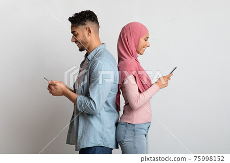 Smartphone Addiction. Cheerful Young Muslim Couple Standing Back To Back Using Smartphones Smartphone Addiction. Cheerful Young Muslim Couple Standing Back To Back Using Smartphones 75998152