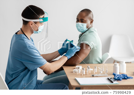 Young doctor in protective mask and uniform gives injection shot to african american patient 75998429