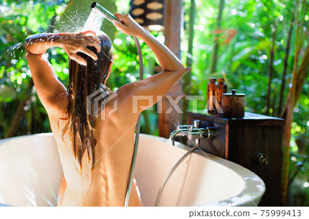 Woman in bath on open-air veranda with garden view Woman in bath on open-air veranda with garden view 75999413