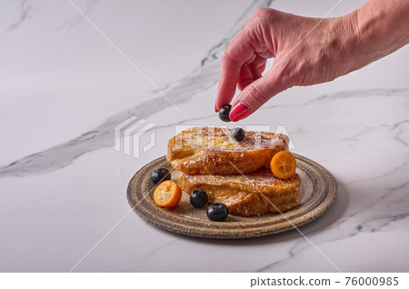 Woman's hand puts a blueberry on homemade traditional Spanish torrijas or French toasts Woman's hand puts a blueberry on homemade traditional Spanish torrijas or French toasts 76000985