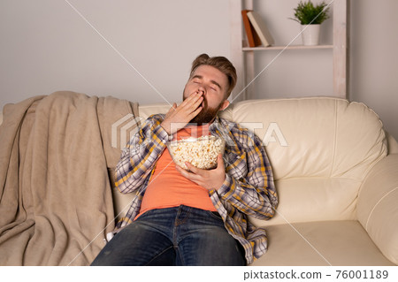 Bearded man watching film or sport games TV eating popcorn in house at night. Cinema, championship and fan concept. Bearded man watching film or sport games TV eating popcorn in house at night. Cinema, championship and fan concept. 76001189