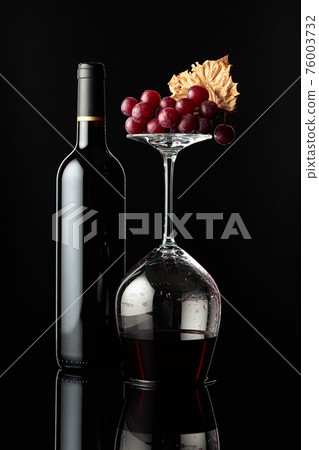 Bottle of red wine and an inverted glass with wine on a black background. Bottle of red wine and an inverted glass with wine on a black background. 76003732