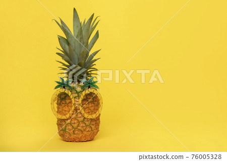 Pineapple with funny pineapple glasses on a yellow background with copy space 76005328