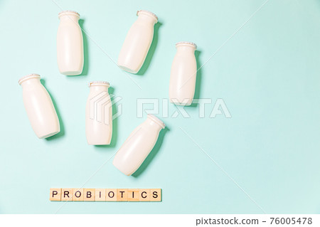 Small bottles with probiotics and prebiotics dairy drink on blue background. Production with biologically active additives. Fermentation and diet healthy food. Bio yogurt with useful microorganisms. Small bottles with probiotics and prebiotics dairy drink on blue background. Production with biologically active additives. Fermentation and diet healthy food. Bio yogurt with useful microorganisms. 76005478