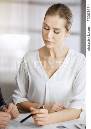 Business people discussing something while sitting in sunny office. Focus at businesswoman while talking to her male colleague 76005684