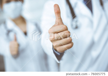 Unknown man-doctor and woman standing straight as a team and showing Ok sign with thumbs up in modern clinic. Medicine concept during Coronavirus pandemic. Covid 2019 76005775
