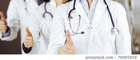 Group of doctors standing as a team with thumbs up in sunny clinic. Good news and Hope for a cure. Medicine concept during Coronavirus pandemic. Covid-2019 Group of doctors standing as a team with thumbs up in sunny clinic. Good news and Hope for a cure. Medicine concept during Coronavirus pandemic. Covid-2019 76005859