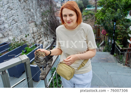 Young european woman caresses Turkish stray cat in Antalya. Young european woman caresses Turkish stray cat in Antalya. 76007306