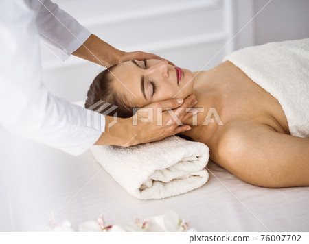 Beautiful brunette woman enjoying facial massage comfortable and bissfulle. Relaxing treatment in medicine and spa center concepts 76007702