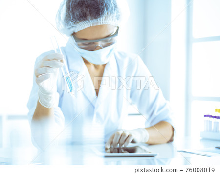 Professional female scientist in protective eyeglasses researching tube with reagents in laboratory. Concepts of medicine and research 76008019