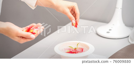 Beautician preparing manicure bath with petals 76009880