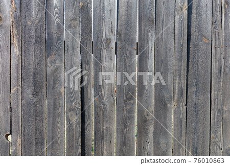 The texture of a gray windy wooden fence made of unpainted wood with rusty nails. A high resolution. 76010863