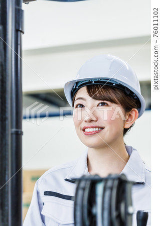 A woman wearing a helmet and operating a forklift 76011102