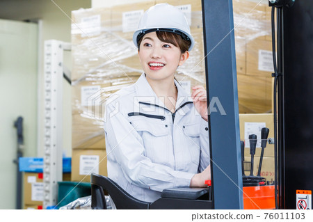 A woman wearing a helmet and operating a forklift A woman wearing a helmet and operating a forklift 76011103
