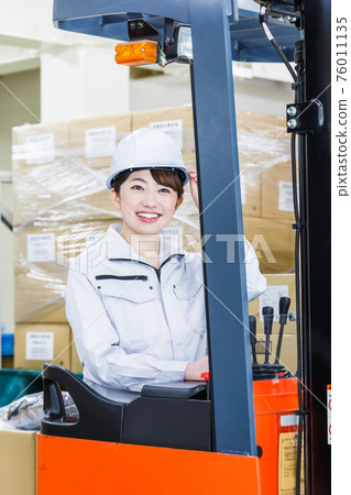 A woman wearing a helmet and operating a forklift A woman wearing a helmet and operating a forklift 76011135