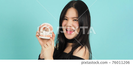 Woman holding dental teeth model or orthodontic model. Asian teenage black hair showing block of teeth for education. Pretty girl with plastic denture in hand. studio background. Oral care concept. 76011206