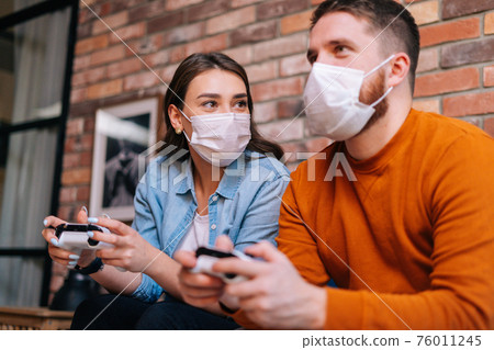 Close-up portrait of happy young couple wearing medical protective masks playing video games on console Close-up portrait of happy young couple wearing medical protective masks playing video games on console 76011245