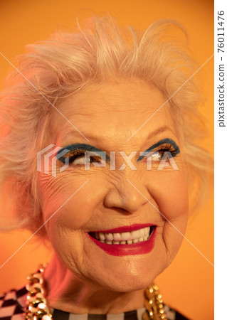 Woman with bright make up and toothy smile gazing away while feeling happy 76011476