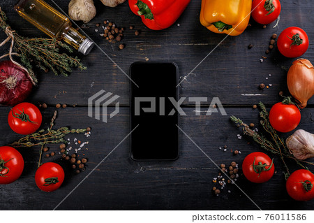 Tomatoes, bell peppers, garlic, olive oil and a cutting board on a black wooden table. Dark contrast food flat lay with vegetables and spices. Black smartphone. Top view. Tomatoes, bell peppers, garlic, olive oil and a cutting board on a black wooden table. Dark contrast food flat lay with vegetables and spices. Black smartphone. Top view. 76011586