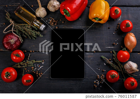 Tomatoes, bell peppers, garlic, olive oil and a cutting board on a black wooden table. Dark contrast background with vegetables and spices. Tablet PC. Top view. Tomatoes, bell peppers, garlic, olive oil and a cutting board on a black wooden table. Dark contrast background with vegetables and spices. Tablet PC. Top view. 76011587