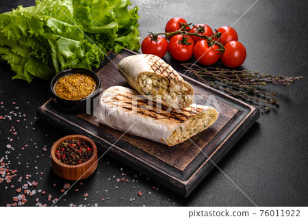 Delicious fresh shawarma with meat and vegetables on a dark concrete table Delicious fresh shawarma with meat and vegetables on a dark concrete table 76011922