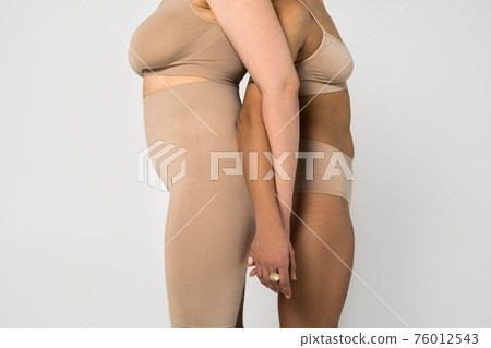 Two girls with different types of figure standing back to back to each other 76012543