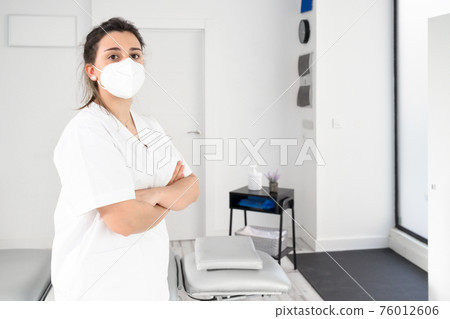 Confident female physiotherapist posing in modern clinic wearing protective face mask during Confident female physiotherapist posing in modern clinic wearing protective face mask during 76012606
