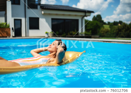 Young woman in swimming pool outdoors in backyard garden, relaxing. 76012706