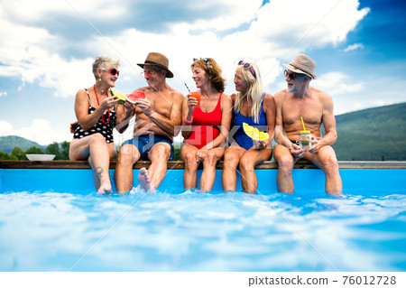Group of cheerful seniors sitting by swimming pool outdoors in backyard. Group of cheerful seniors sitting by swimming pool outdoors in backyard. 76012728