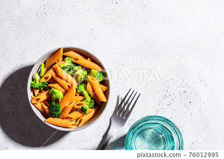 Red lentil pasta with broccoli in gray bowl, top view, copy space. Healthy vegan pasta with vegetables. 76012995