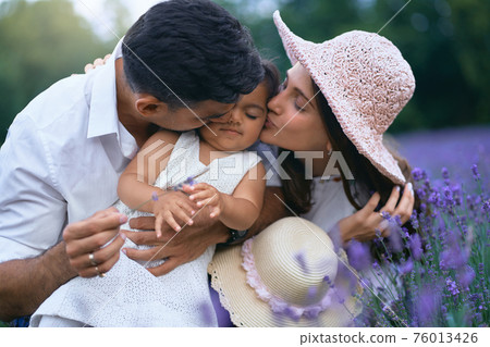Young parents kissing little daughter in lavender field 76013426