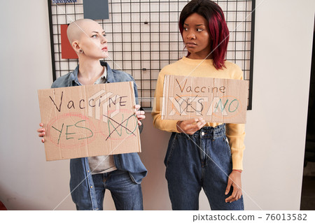 Girls looking at each other while showing cupboard posters about vaccine 76013582