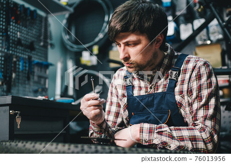 Bike shop mechanic fixing bicycle wheel in workshop. Serviceman repair, maintenance cycle. Velocipede repairing bicycle in bike shop. Bicycle repair service concept. Environmentally friendly vehicles 76013956