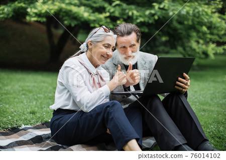 Happy mature couple using laptop for video call at park Happy mature couple using laptop for video call at park 76014102