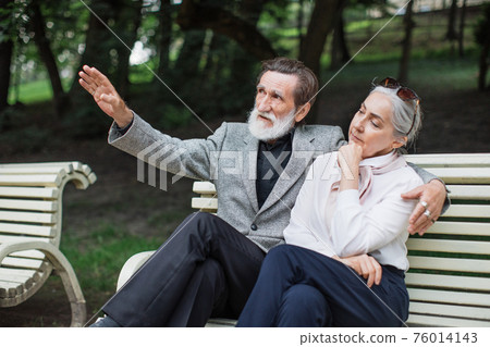 Stylish elderly couple sitting in embrace on bench Stylish elderly couple sitting in embrace on bench 76014143