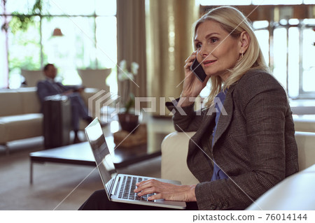 Elelgant woman in the middle of a phone call enjoying the comfort of a waiting lounge Elelgant woman in the middle of a phone call enjoying the comfort of a waiting lounge 76014144