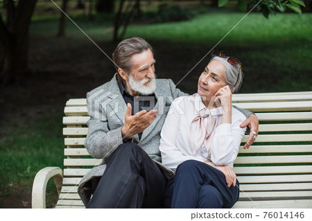 Romantic aged couple sitting on wooden bench at green park Romantic aged couple sitting on wooden bench at green park 76014146
