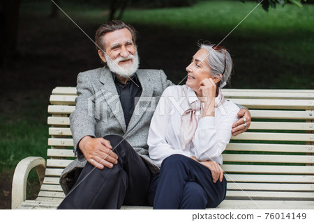 Romantic aged couple sitting on wooden bench at green park 76014149