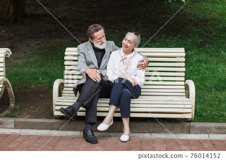 Senior couple chatting and hugging on bench at park Senior couple chatting and hugging on bench at park 76014152