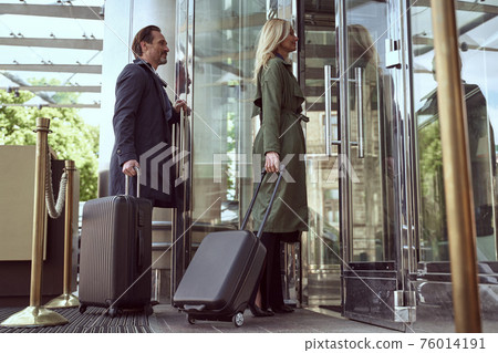 Gladsome man holding a hotel door open for his pretty wife 76014191