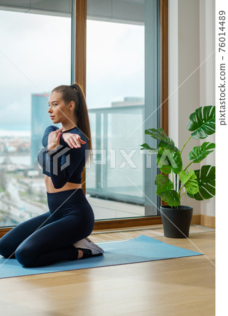 Brunette with ponytail practices yoga pose on balcony Brunette with ponytail practices yoga pose on balcony 76014489