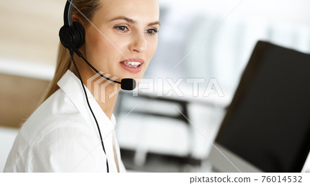 Blond female customer service representative is consulting clients online using headset. Call center and business concept 76014532